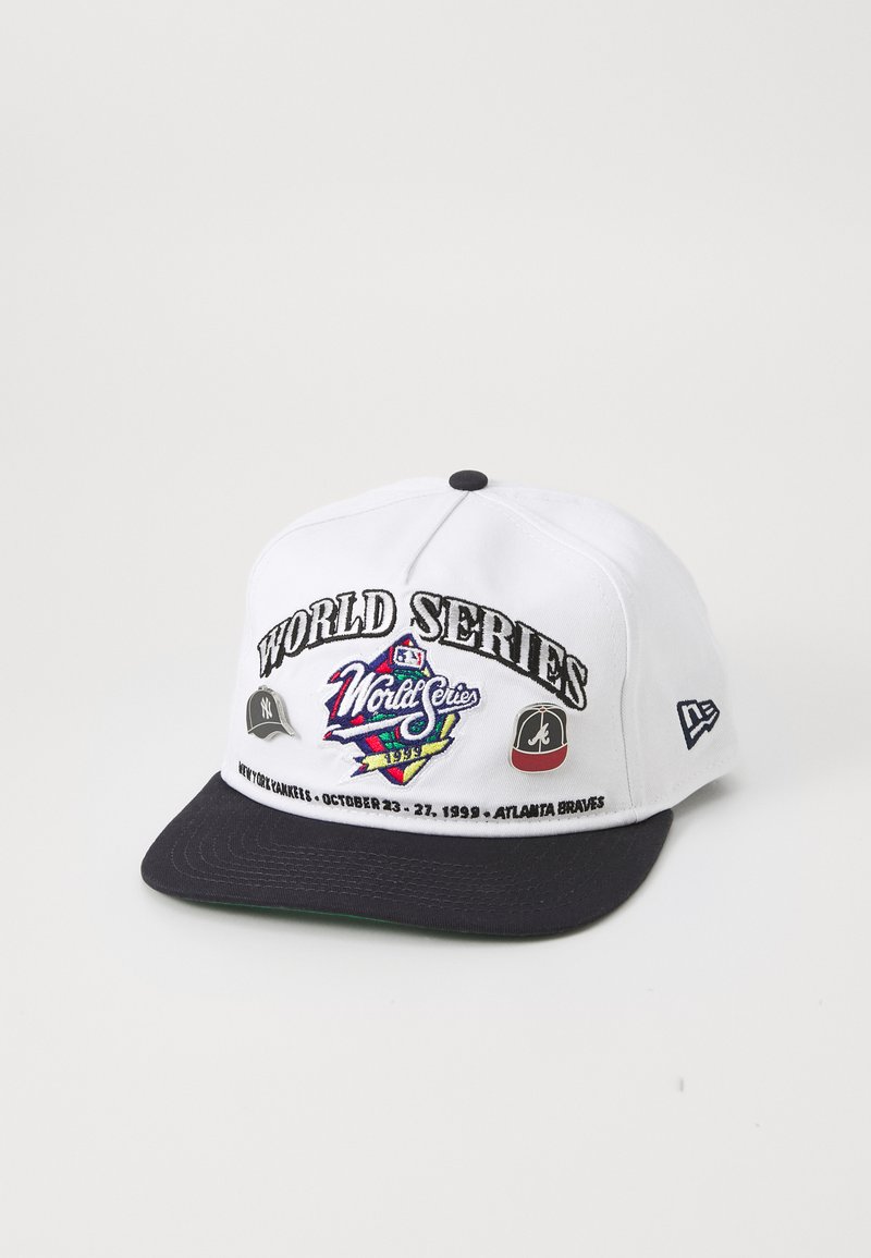 Boné de basebol branco com aba azul-marinha, bordado com o texto "WORLD SERIES", logos das equipas e datas do evento de 1999. Apresenta um fecho de pressão em plástico.