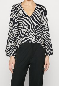 Blouse à imprimé zèbre noir et blanc avec un col en V, des manches longues et une coupe décontractée, associée à un pantalon noir avec des poches latérales.