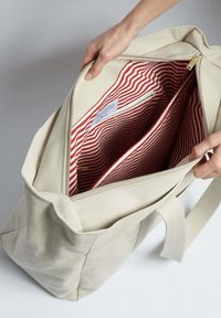 Beige plátěná taška s červenobílou pruhovanou podšívkou, obsahující několik přihrádek a zlatý zip.}}