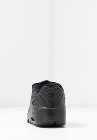 Μαύρο αθλητικό παπούτσι με υφή στο πάνω μέρος, μαλακή κολαρίνα και εμφανές λογότυπο. Σχηματισμός καμπύλης με μαξιλαρωμένη σόλα και καουτσούκ σόλα.