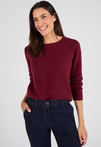 Maglione bordeaux con motivo a diamante testurizzato, scollo rotondo e maniche lunghe, abbinato a jeans in denim blu scuro.