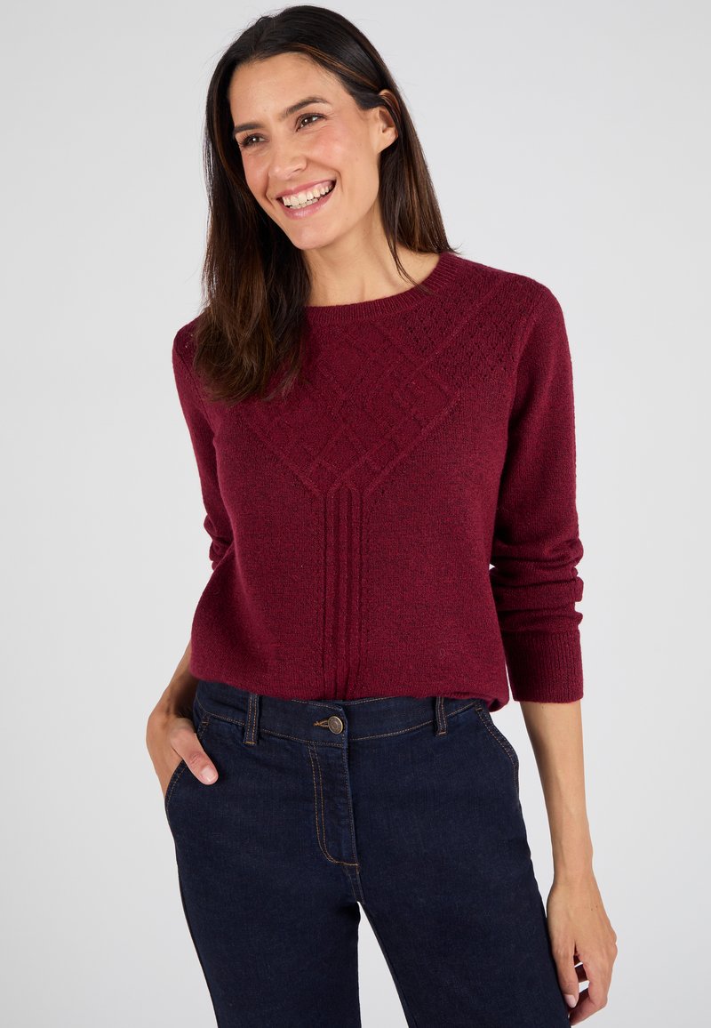 Maglione bordeaux con motivo a diamante testurizzato, scollo rotondo e maniche lunghe, abbinato a jeans in denim blu scuro.