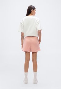 Sweat-shirt blanc à manches courtes associé à un short rose à taille élastique, présentant un style simple et un design minimaliste. Baskets blanches et chaussettes texturées.