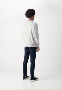 Light grey sweatshirt with ribbed cuffs, paired with navy slim-fit pants and black sneakers. Simple design, no visible logos or patterns.