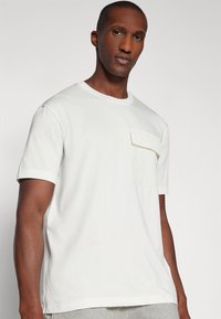 Camiseta de algodón blanca de manga corta, con escote redondo y un detalle de bolsillo texturizado en el lado izquierdo del pecho. Corte regular.