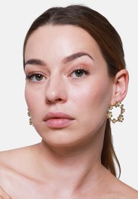 Orecchini a cerchio dorati con un design floreale, caratterizzati da piccoli fiori attorno al bordo. Superficie liscia e lucida e dettagli intricati.