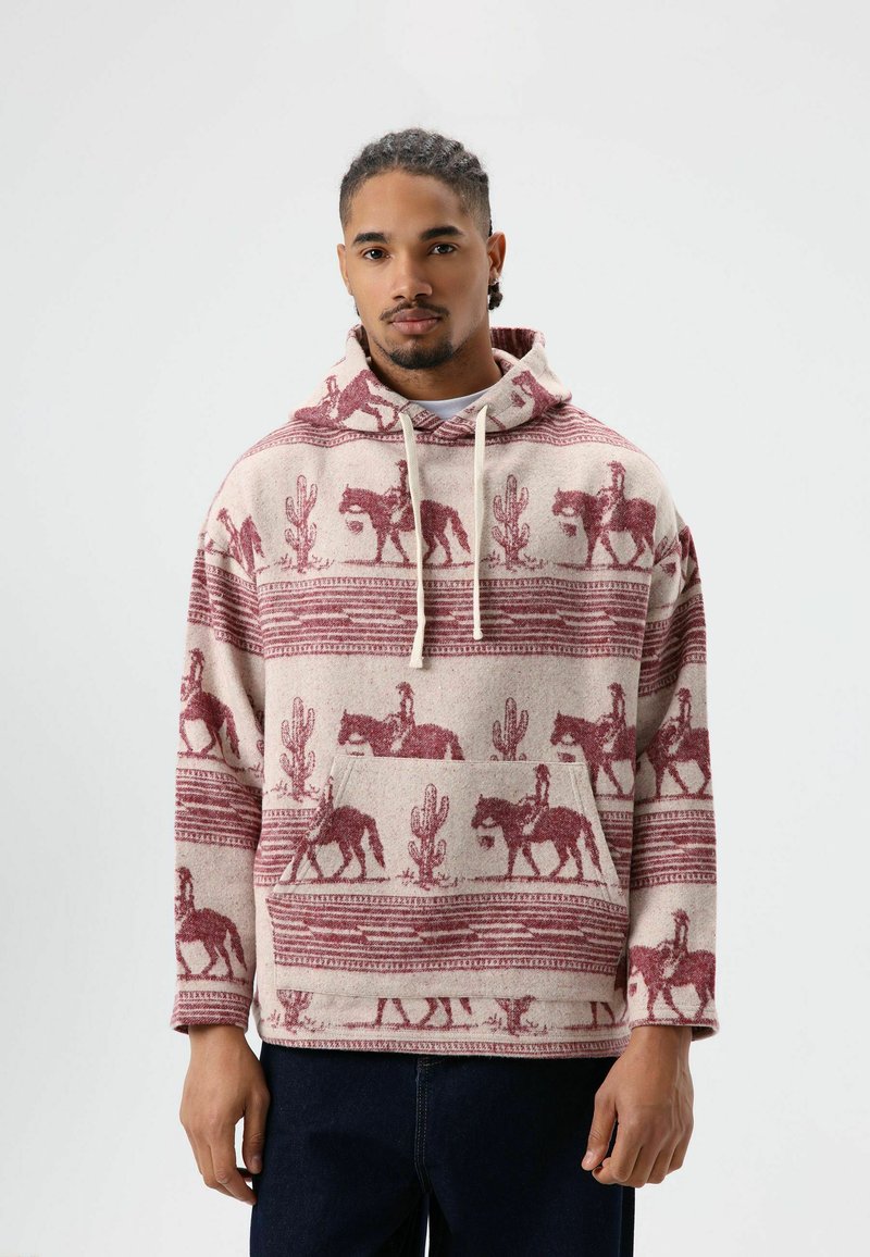 Pull-over à capuche avec une base crème ornée de motifs de cow-boy et de cactus bordeaux. Tissu doux, poche avant et cordon de serrage ajustable.