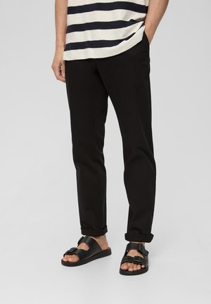 Pantalones ajustados negros, sandalias negras con dos hebillas y una camisa de rayas en azul marino y blanco. Tejido suave y dobladillos de los pantalones enrollados.