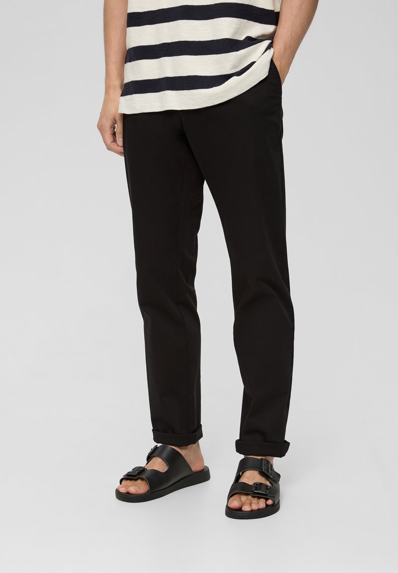 Pantalones ajustados negros, sandalias negras con dos hebillas y una camisa de rayas en azul marino y blanco. Tejido suave y dobladillos de los pantalones enrollados.