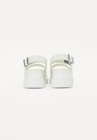 Sandali bianchi con suola spessa, dotati di due cinturini regolabili, chiusura con fibbia e design senza tacco. Realizzati in materiale liscio e flessibile.