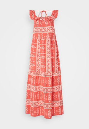 Robe maxi en tissu corail avec des motifs géométriques blancs, épaules volantées et un détail noué dans le dos pour un ajustement réglable.