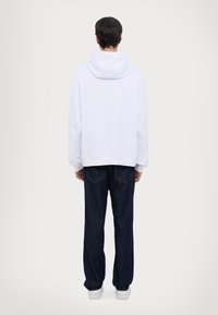 Hvid hættetr�øje med løs pasform, ribbede manchetter og kant, parret med mørkeblå straight-leg jeans og hvide sneakers.