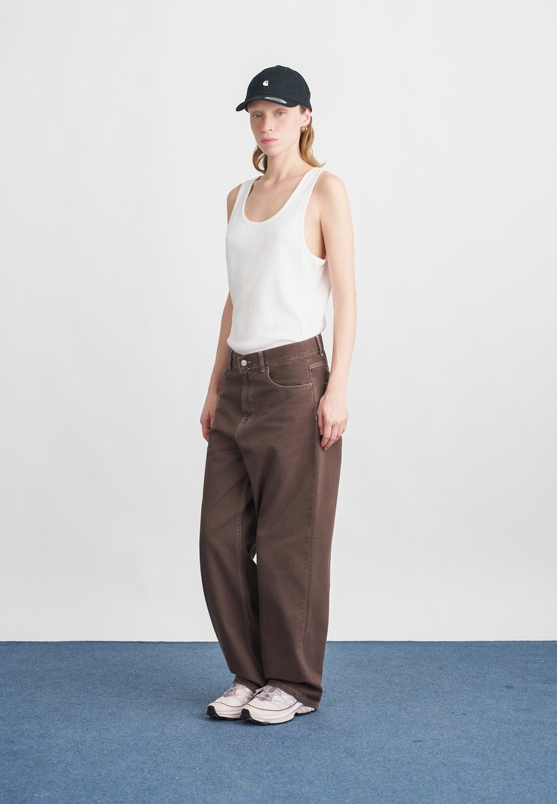 Weißes Tanktop, braune weite Jeans, schwarze Cap und helle Sneakers. Glattes Material und einfaches Design mit sichtbaren Nähten und Taschen.