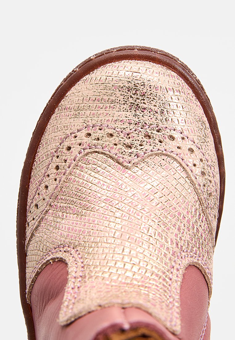 Kinderschuh aus pinkem Leder mit strukturiertem, metallischem Finish und brauner Sohle, Nahaufnahme, die die detaillierte Nahtführung und die Perforationsmuster zeigt.