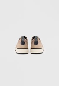 Beige Wildlederschuhe mit Gummisohle, ausgestattet mit einem strukturierten schwarzen Fersenelement und einem hexagonalen Logo-Akzent. Minimalistisches Design mit runder Form.