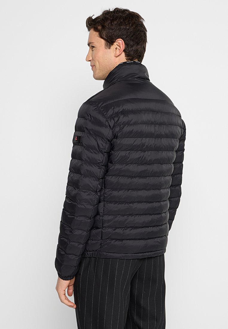 Pufferjack in het zwart, met een gewatteerd ontwerp, hoge kraag en verstelbare manchetten. Er is een klein logo op de linkermouw.
