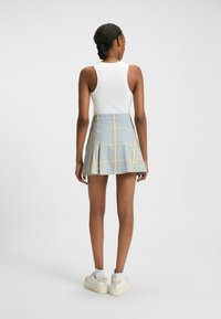 Lichtblauwe geruite mini-jurk met plooien, gecombineerd met een witte tanktop. Heeft een aansluitende tailleband en een gladde stofstructuur.