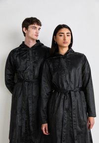 Black satin hooded coats with belts, featuring a smooth texture and subtle sheen, worn by two models standing side by side.