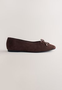 Ballerine en daim marron avec un petit nœud et des lacets à embouts métalliques à l'avant, avec une semelle noire basse et un bout arrondi.