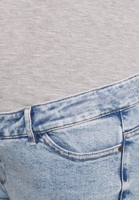 T-shirt cinza claro parcialmente dentro de jeans de denim azul claro. Os jeans apresentam um design clássico de cinco bolsos e um efeito desbotado.