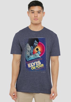 Young man wearing a dark blue T-shirt featuring a colorful Elvis Presley "Elvis On Tour" concert graphic with microphone and vibrant background.