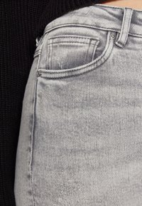 Lys grå denimjeans med en falmet finish og subtile skader, som har tradisjonelle lommer og en solid livlinje.