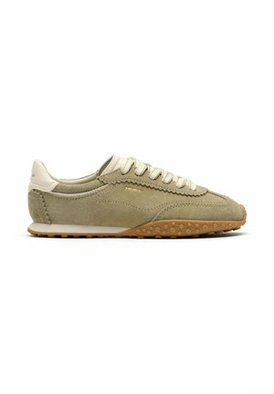 Zapatilla deportiva de ante marrón claro con cordones beige, lengüeta blanca en el talón y suela de goma con agarre texturizado, vista lateral hacia la derecha.
