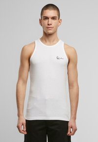 Weißes ärmelloses Tank-Top mit gerippter Textur, das über einen runden Halsausschnitt und ein kleines schwarzes Logo auf der Brust verfügt.