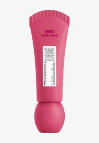 Tube en plastique rose avec une base arrondie, un capuchon strié et du texte imprimé. Contient une étiquette de produit avec des détails sur les ingrédients et l'utilisation.