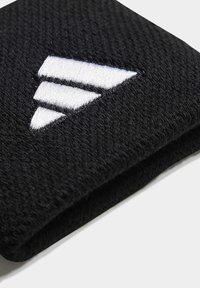 Melnas auduma rokassprādze ar teksturētu adītu virsmu, kurai ir izteiksmīgs balts izšūts trīsstūra logos. Kompakts un salokāms dizains.