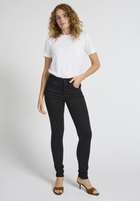 Blugi negri skinny cu textură netedă și buzunare tradiționale, asortați cu un tricou alb simplu și sandale maro cu vârf deschis.