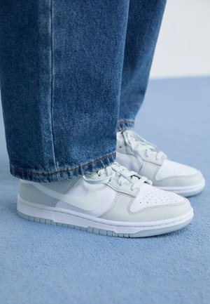 Nike sneakers i hvidt og lysegråt læder med perforeret tå, flade snørebånd og gummisål, kombineret med blå denimjeans.
