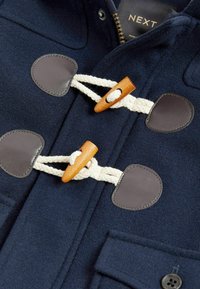 Marine wolcoat met tan lederen patches en houten toggles. Bevat gevlochten touwsluitingen en een knoopsluiting op het voorvak.