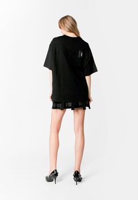 Camisa oversized negra con capas texturizadas, mangas cortas y un detalle de dobladillo transparente. Terminada con un sutil acento de bolsillo en la parte posterior.