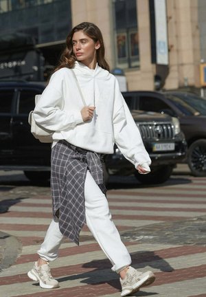 Biała, oversize bluza z kapturem i kieszenią kangurką, zestawiona z białymi dresami. Szara koszula w kratę związana wokół talii. Beżowe sneakersy dopełniają całość.