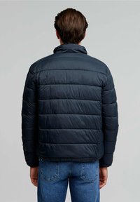 Veste matelassée bleu marine avec un design trapézoïdal et un col haut, présentant des coutures horizontales et une texture lisse et brillante.