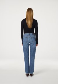 Hoogwaardige blauwe denim jeans met een relaxed fit, vijf-pocket ontwerp en zichtbare stiksels op de achterzakken. Model draagt een zwart top.