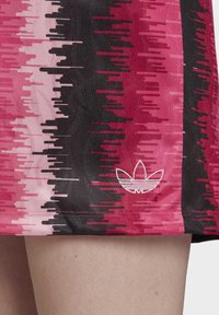 Růžová a černá sukně s vzorem v gradientním designu a horizontálními pruhy; na spodním lemu je vyšívané bílé logo.