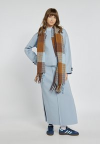 Jasnoniebieski sweter i pasująca długa spódnica, zestawione z brązowym i niebieskim szalikiem w kratę. Granatowe sneakersy z białymi akcentami dopełniają całość.