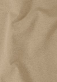 Texture de tissu beige montrant un tricot fin avec de doux plis et des ombres légères, mettant en valeur la surface lisse et uniforme du matériau.