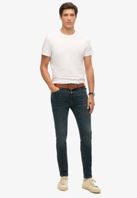 Camiseta blanca de algodón, jeans slim-fit azules, cinturón de cuero marrón, zapatillas beige; colores neutros, diseño simple, detalle de costura mínima.
