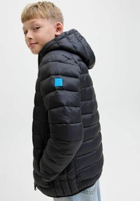 Svart puffjacka med huva, quiltad design, med en blå logopatch på övre vänstra ärmen. Mjuk, slät textur.