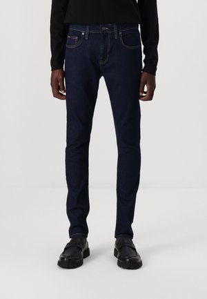 Jeans negri închis, cu croi slim, din denim cu accente de cusături deschise, buzunare frontale și închidere cu nasture. Purtați cu pantofi negri.