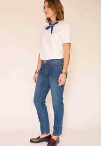 Jean en denim bleu à coupe droite, porté avec un t-shirt blanc et un foulard bleu autour du cou ; associé à des mocassins bordeaux. Design simple.