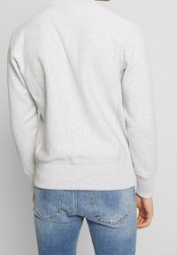 Hellgrauer Sweatshirt mit strukturiertem Finish, Rundhalsausschnitt und gerippten Bündchen, kombiniert mit blauen Jeans mit Gesäßtaschen und verblasstem Design.