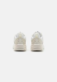 Sneaker sportive bianche con una tomaia in tessuto texture, collare imbottito, ammortizzazione del tallone prominente e suola leggera e rigata.