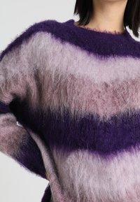 Pull en tissu texturé, rayé violet et rose. Doté d'un col rond et d'une coupe ample, mettant en valeur des couleurs douces et superposées.