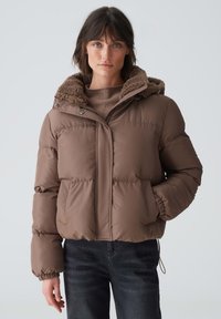 Brown puffer jacket with a textured, fleece-lined hood. Features a zip closure, side pockets, and elastic cuffs. Cropped design.