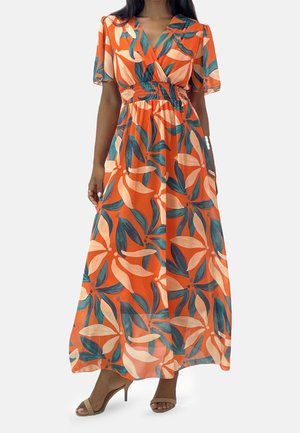 Femme portant une robe maxi orange avec de grands motifs de feuilles tropicales roses et vertes, des manches courtes volantées et des sandales beiges à talons hauts.