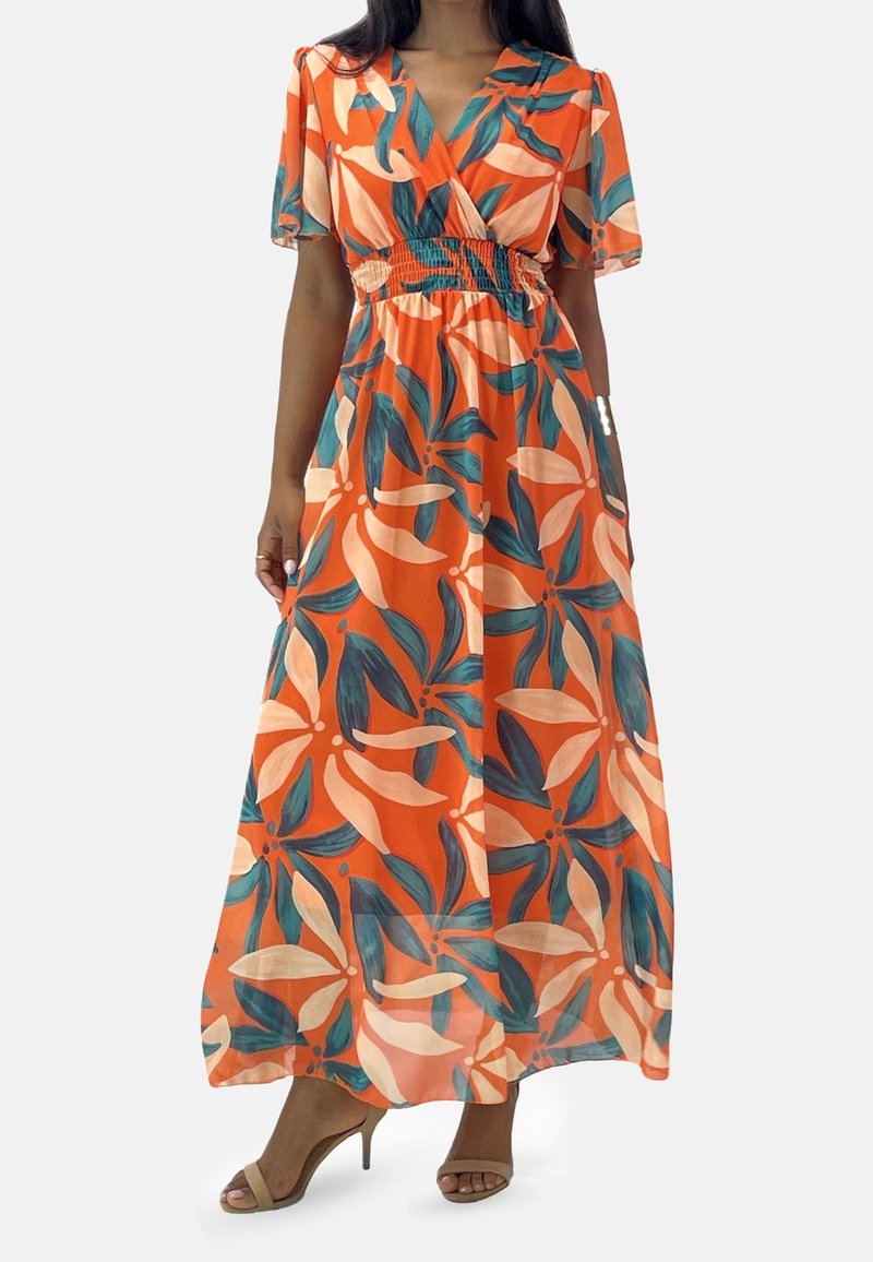 Femme portant une robe maxi orange avec de grands motifs de feuilles tropicales roses et vertes, des manches courtes volantées et des sandales beiges à talons hauts.